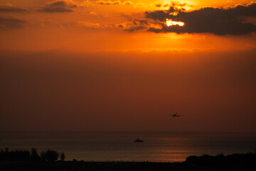 Fototapeta premium Back view silhouette of airplane landing at the airport at sunny orange and purple sunset. Runway