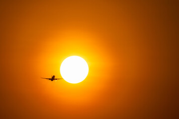 Back view silhouette of airplane take-off into sunny orange and purple sunset
