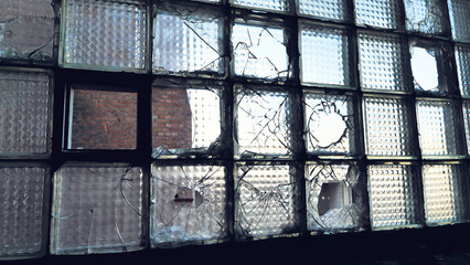 A wall of glass blocks, many of which are broken or cracked. A scene from an abandoned or neglected...