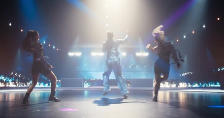 Pop Artist Runs to Perform on a Vibrant Stage with Two Energetic Female Dancers, Entertaining a Large Audience in a Concert Hall. Performers Dancing a Synchronized Choreography Routine