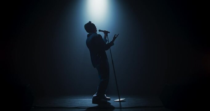Pop Artist Performing Live Concert on Stage, Illuminated by a Spotlight. Epic Cinematic Performance Captures Artist's Passion and Energy. Dark Background Creating a Dramatic Lonely Scene