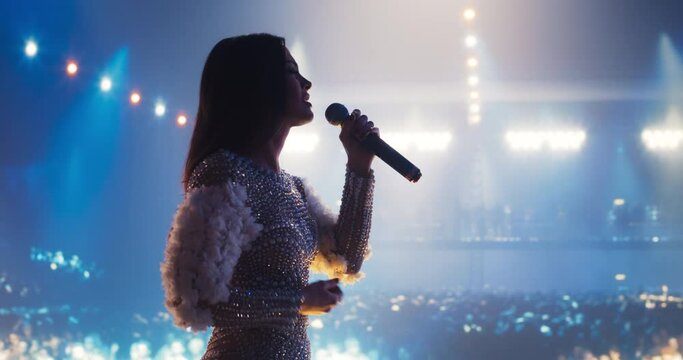 Lead Singer of a Pop Band Performing on a Live Concert Stage. Portrait of a Young Fashionable Female Wearing a Striking Bodysuit Covered with White Pearls, Singing a Hit Song into the Microphone