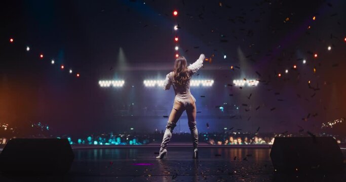 Pop Music Diva Performing a Live Concert on Stage, Surrounded by Falling Confetti and Dynamic Lighting. Musician Captivating the Audience with Her Outfit and Energetic Show. Footage From the Back