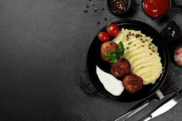 Fried cutlets with mashed potatoes, tomatoes and herbs. Black plate on a black background