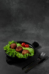 Fried cutlets on a lettuce leaf with tomato on a black background