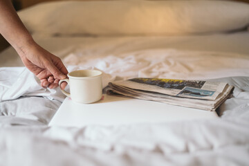 Bedside Reading And Coffee.
A Hand Reaching For A Coffee Mug Next To A Newspaper On A Bed, Illustrating A Calm Morning.