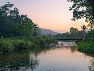 Obraz premium A peaceful river scene with clear water, lush green banks, and a small wooden bridge crossing the river. The sky is a soft pastel color as the sun begins to set.