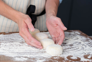 Hands of a female chef preparing homemade syrniki (cottage cheese pancakes)  by coating them in flour on a wooden board before frying. Home cooking, traditional recipes, and culinary preparation.