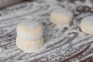 Hands of a female chef preparing homemade syrniki (cottage cheese pancakes)  by coating them in flour on a wooden board before frying. Home cooking, traditional recipes, and culinary preparation.