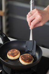 Hands of a female chef frying and baking homemade syrniki in a pan, sizzling in oil. Concept of home cooking, traditional recipes, and culinary preparation.