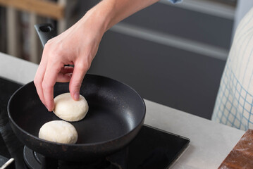 Hands of a female chef frying and baking homemade syrniki in a pan, sizzling in oil. Concept of home cooking, traditional recipes, and culinary preparation.