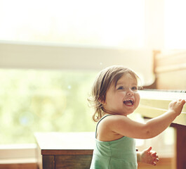 Girl, toddler and playful on piano in home for musical development, learning and growth of motor skills or creativity. Child, instrument and playing in house for entertainment, education and sound.