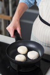 Hands of a female chef frying and baking homemade syrniki in a pan, sizzling in oil. Concept of home cooking, traditional recipes, and culinary preparation.