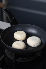 Hands of a female chef frying and baking homemade syrniki in a pan, sizzling in oil. Concept of home cooking, traditional recipes, and culinary preparation.