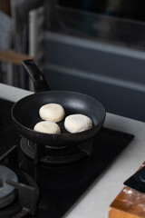 Hands of a female chef frying and baking homemade syrniki in a pan, sizzling in oil. Concept of home cooking, traditional recipes, and culinary preparation.