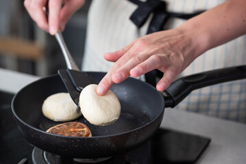 Hands of a female chef frying and baking homemade syrniki in a pan, sizzling in oil. Concept of home cooking, traditional recipes, and culinary preparation.