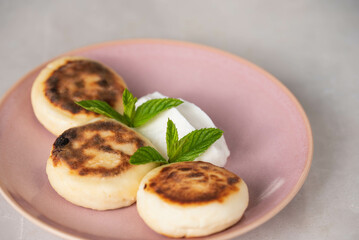 Syrniki (cottage cheese pancakes) on a plate, garnished with sour cream and mint, ready to be enjoyed for breakfast. Concept of home cooking, traditional recipes, and delicious morning meals.