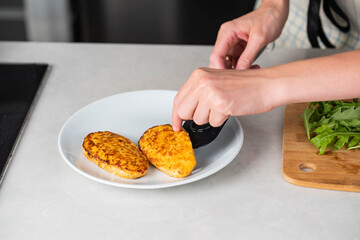 Fish cutlets being placed on a plate and garnished with arugula salad and cherry tomatoes. Concept of home cooking, traditional healthy food recipes, and culinary presentation.