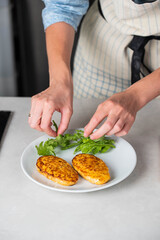 Fish cutlets being placed on a plate and garnished with arugula salad and cherry tomatoes. Concept of home cooking, traditional healthy food recipes, and culinary presentation.