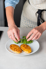 Fish cutlets being placed on a plate and garnished with arugula salad and cherry tomatoes. Concept of home cooking, traditional healthy food recipes, and culinary presentation.
