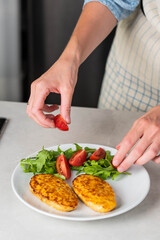 Fish cutlets being placed on a plate and garnished with arugula salad and cherry tomatoes. Concept of home cooking, traditional healthy food recipes, and culinary presentation.