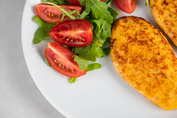 Fish cutlets being placed on a plate and garnished with arugula salad and cherry tomatoes. Concept of home cooking, traditional healthy food recipes, and culinary presentation.