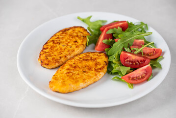 Fish cutlets being placed on a plate and garnished with arugula salad and cherry tomatoes. Concept of home cooking, traditional healthy food recipes, and culinary presentation.