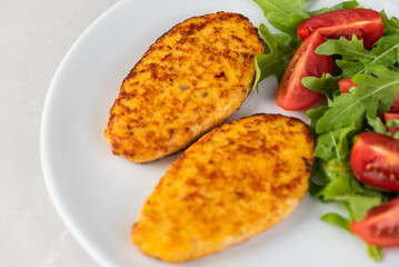 Fish cutlets being placed on a plate and garnished with arugula salad and cherry tomatoes. Concept of home cooking, traditional healthy food recipes, and culinary presentation.
