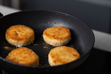 Meatballs or small meat patties cutlets sizzling in oil while frying in a pan on the stove. Concept of home cooking, traditional recipes, and culinary preparation