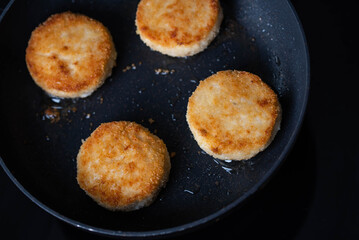 Meatballs or small meat patties cutlets sizzling in oil while frying in a pan on the stove. Concept of home cooking, traditional recipes, and culinary preparation
