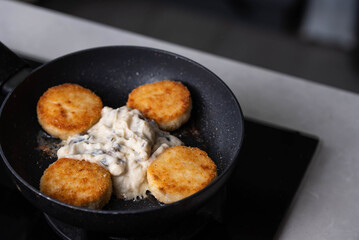 Meatballs or small meat patties cutlets sizzling in oil while frying in white sauce in a pan on the stove. Home cooking, traditional recipes, and culinary preparation