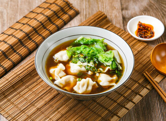 Beef dumplings soup with chilli sauce, spring onion, wooden spoon, and chopsticks served in dish isolated on mat side view of taiwanese food