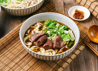 Classic Beef Cheek Noodles with chilli sauce, spring onion, wooden spoon, and chopsticks served in dish isolated on mat side view of taiwanese food