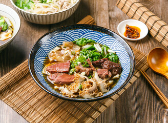 Five Star Beef Noodles with chilli sauce, spring onion, wooden spoon, and chopsticks served in dish isolated on mat side view of taiwanese food