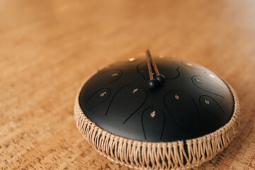 Closeup of black glucophone with professional sticks on floor. Close-up of musical instrument, drum with metal tongue on wooden background. Tool for meditation, relaxation with deep magical sound.