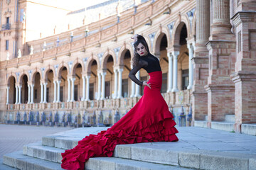 Beautiful woman dancing flamenco in a square in Seville, Spain. She is wearing a typical red and...