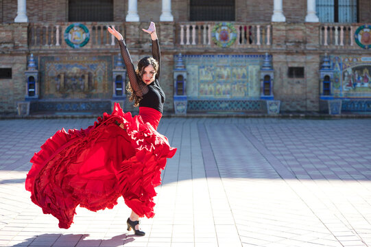Beautiful woman dancing flamenco in a square in Seville, Spain. She is wearing a typical red and black gypsy dress and dancing flamenco with a lot of art. Flamenco, cultural heritage of humanity.