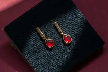 Golden earrings with red stones placed on a black box, set against a red background.