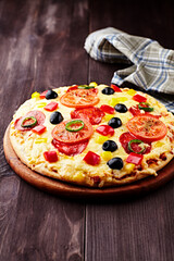 Pizza with salami, black olives, tomatoes and red, yellow and jalapeno pepper. Dark wooden background. Copy space.
