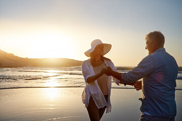 Mature, happy couple and dancing with beach in sunset for love, bonding or support in nature. Man, woman or lovers enjoying romance or holding hands for outdoor holiday or summer by ocean coast
