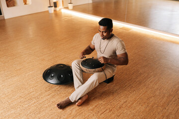 Remote top view of happy African man in trance playing meditative instrument tank drum sitting...
