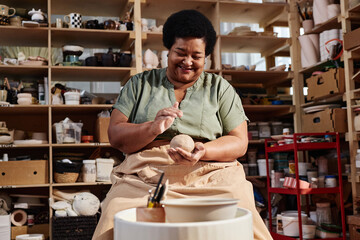 Candid portrait of smiling Black senior woman enjoying pottery class in art studio lit by sunlight copy space