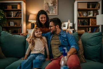 Smiling parents with their daughter enjoying quality time on the living room sofa
