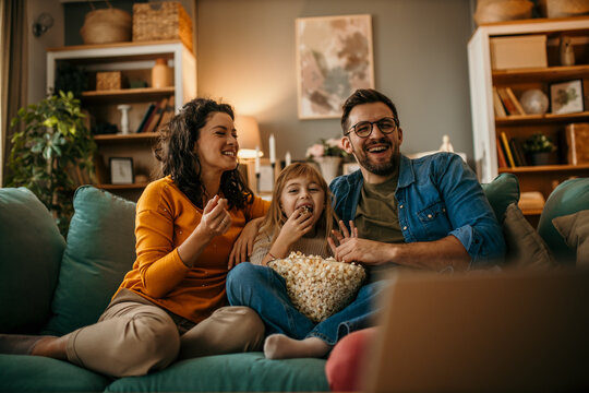 Smiling Caucasian family sitting on the couch and watching a comedy on the TV