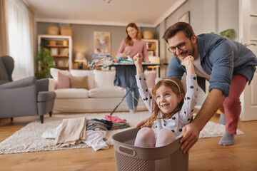 Little girl and dad laughing while playing with the laundry basket in living room