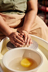 Vertical closeup of unrecognizable Black woman carefully shaping clay on pottery wheel enjoying ceramics class in sunlight