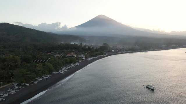 Aerial pan over ocean at sunset with volcano Agung in Amed, Bali