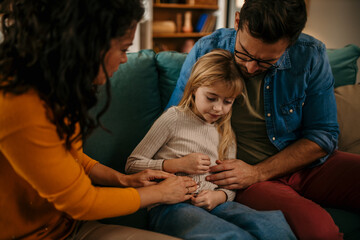 Worried father and mother consoling their little girl who is having stomachache at home