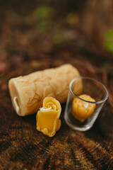 Handmade candles from natural beeswax in the shape of flowers in the glass candle holders on an old stump in the forest. Hobby. Artistic photo of beekeeping products against the backdrop of nature