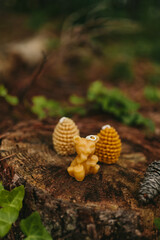Handmade candles from natural beeswax in the shape of bear,  pine cones on an old stump in the forest. Hobby. Artistic photo of beekeeping products against the backdrop of nature